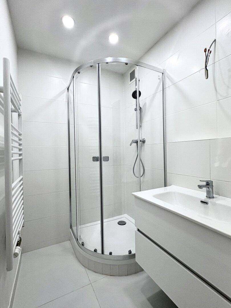 Modernes Badezimmer mit Eckdusche, weißen Fliesen und elegantem Waschtisch.