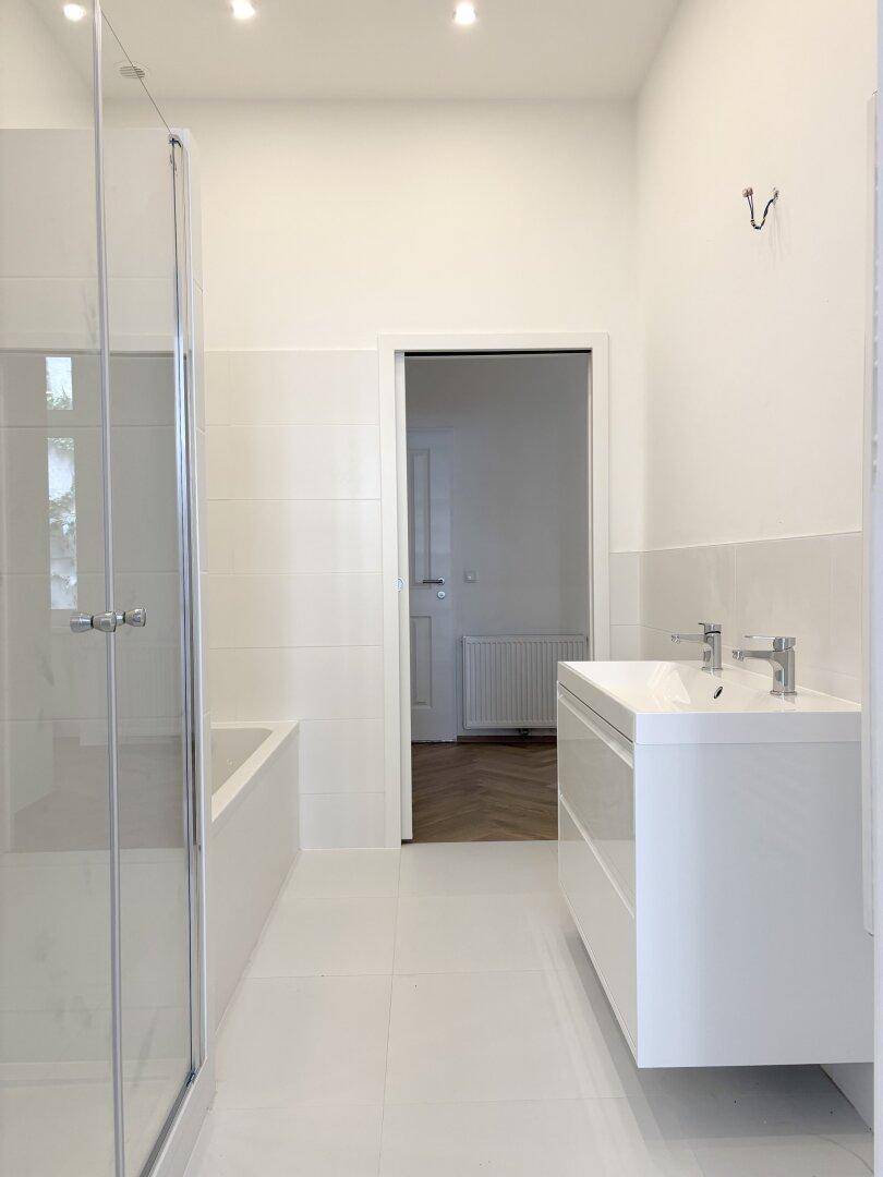 Modernes, helles Badezimmer mit weißem Fliesenboden, Duschkabine und Badewanne.