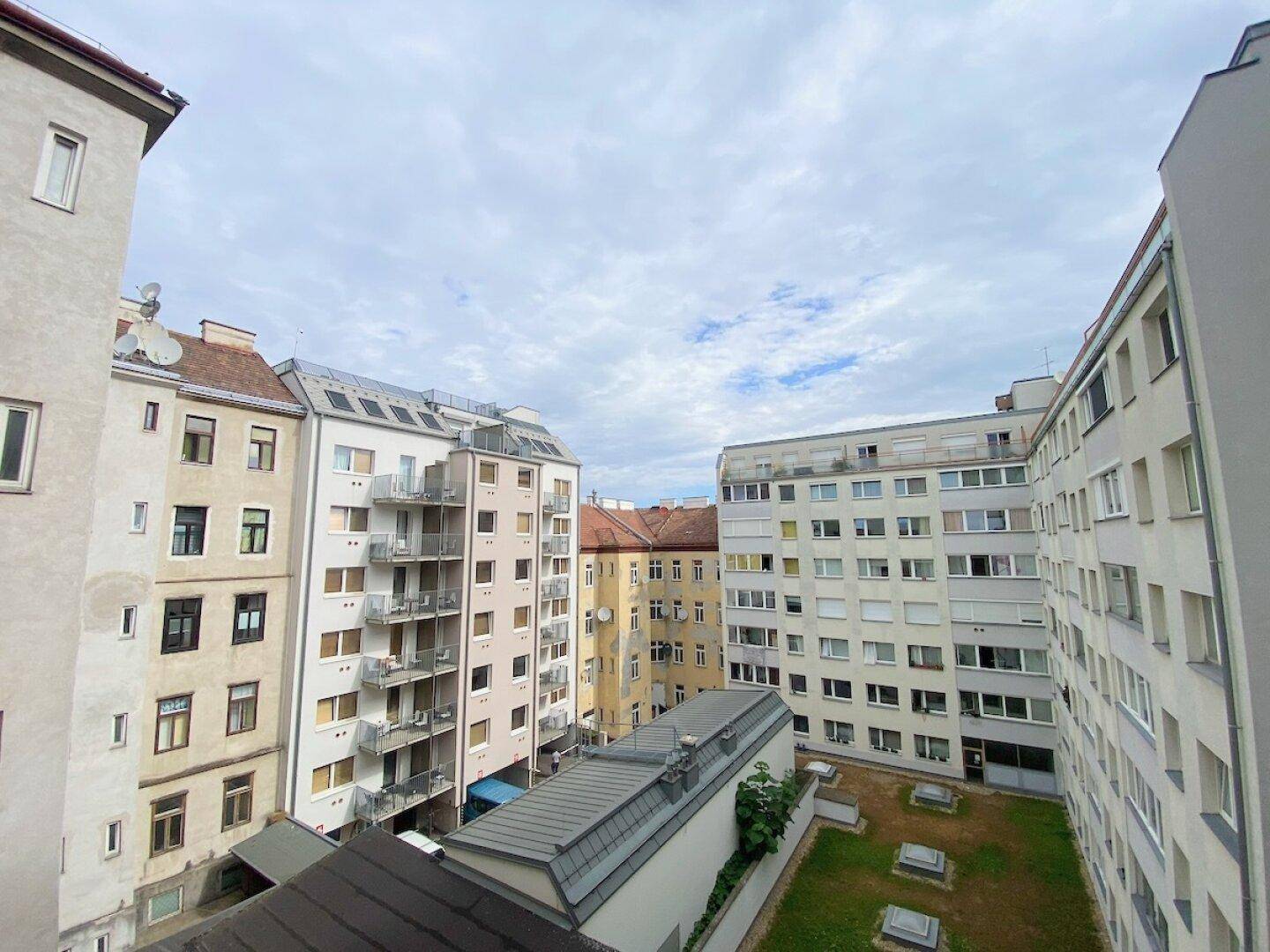 Blick auf den begrünten Innenhof, umgeben von mehreren Wohngebäuden, unter einem bewölkten Himmel.