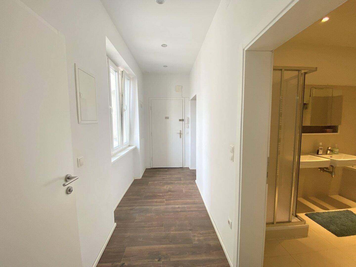 Langer Flur mit Holzfußboden, Einbaustrahlern und Zugang zu verschiedenen Räumen, inklusive Badezimmer.
