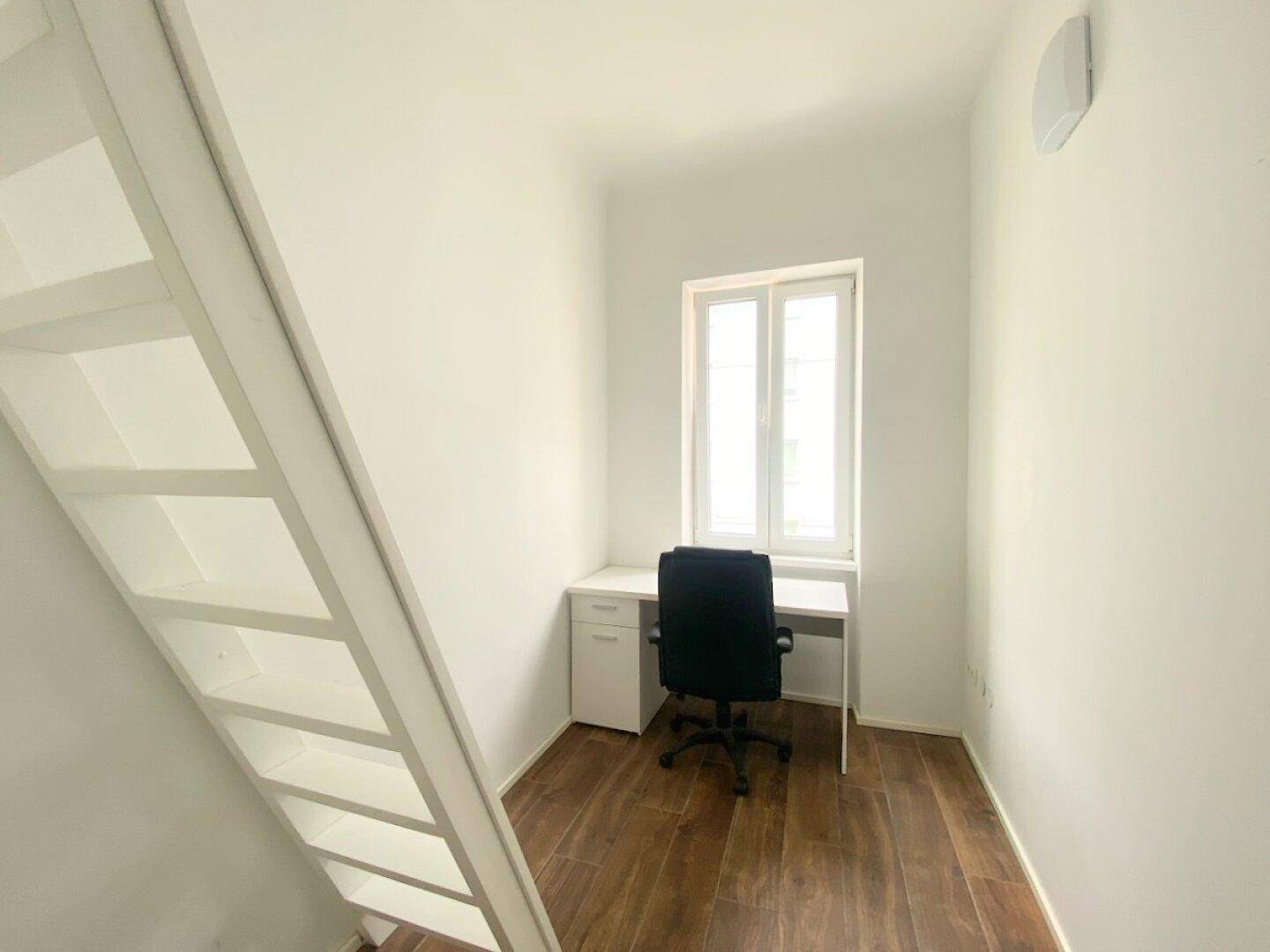 Kompakter Arbeitsbereich mit Schreibtisch, Stuhl und Fenster, ideal für konzentriertes Arbeiten, auf Holzfußboden.