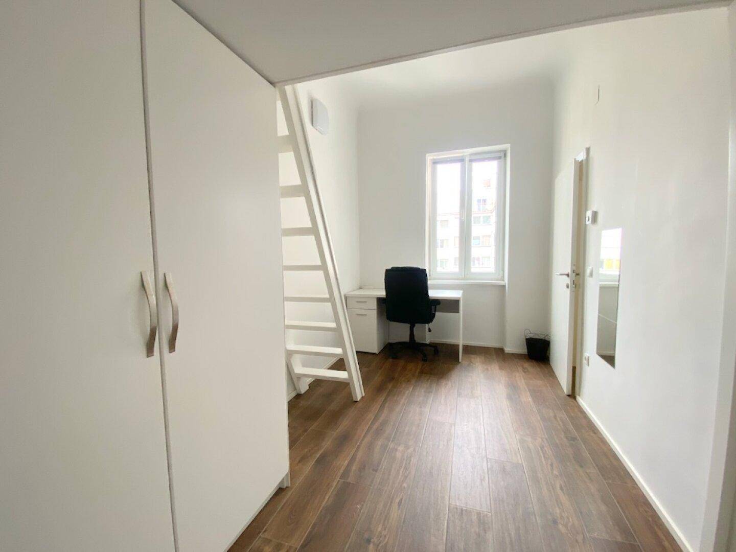 Heller Arbeitsbereich mit Schreibtisch, Stuhl und Fenster, ergänzt durch einen Kleiderschrank und Holzfußboden.
