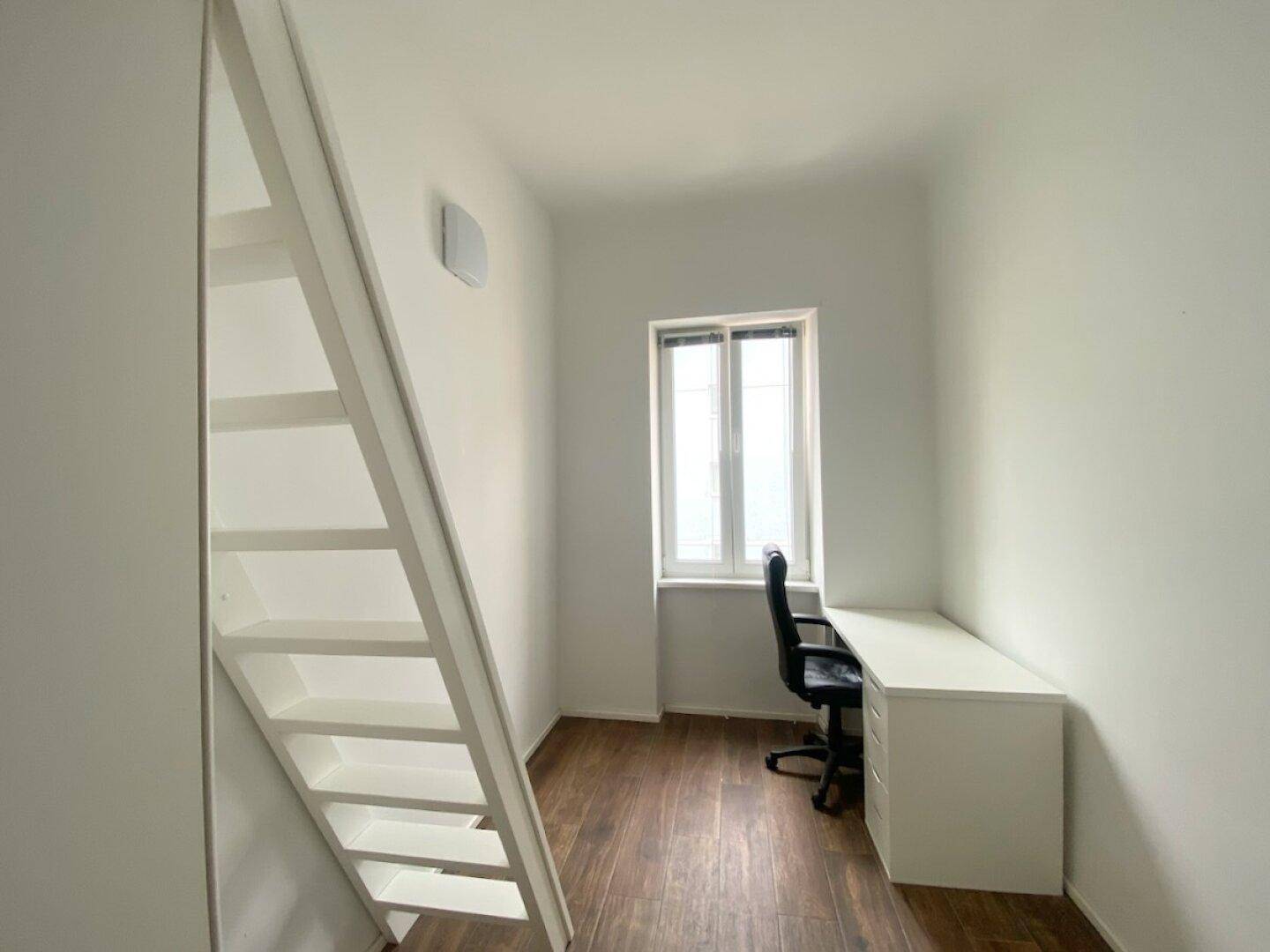 Heller Arbeitsplatz mit Schreibtisch und Fenster, ergänzt durch eine Leiter zum Hochbett, auf Holzfußboden.
