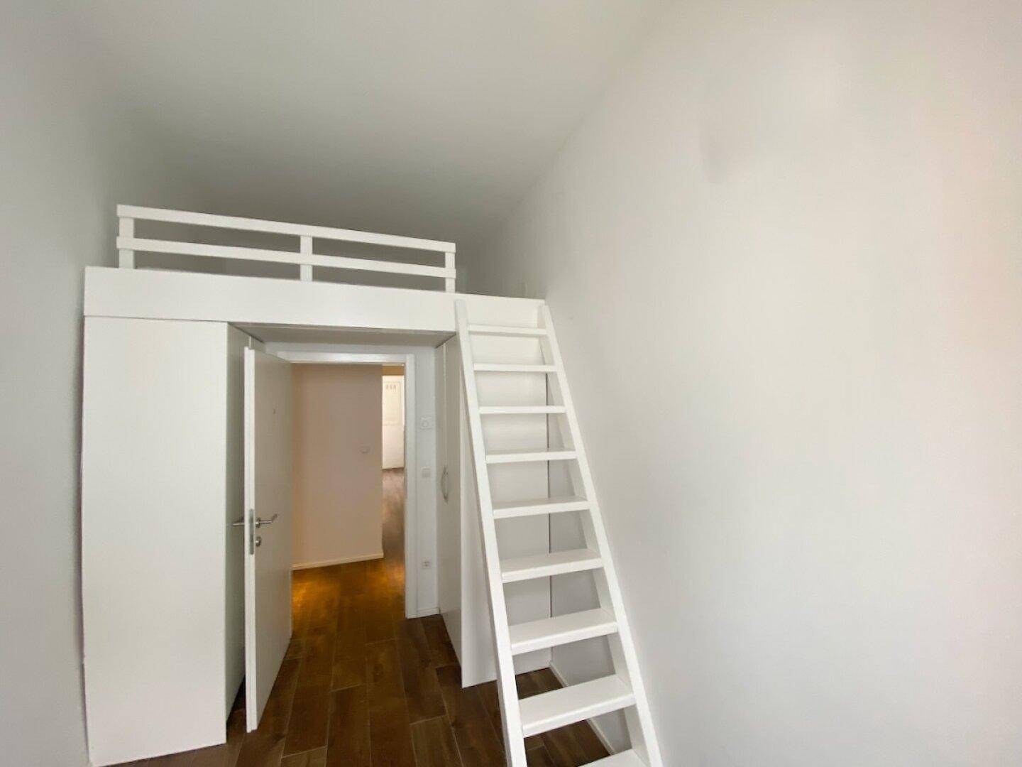 Zimmer mit Hochbett und Leiter, das durch eine offene Tür mit dem Flur verbunden ist, auf Holzfußboden.