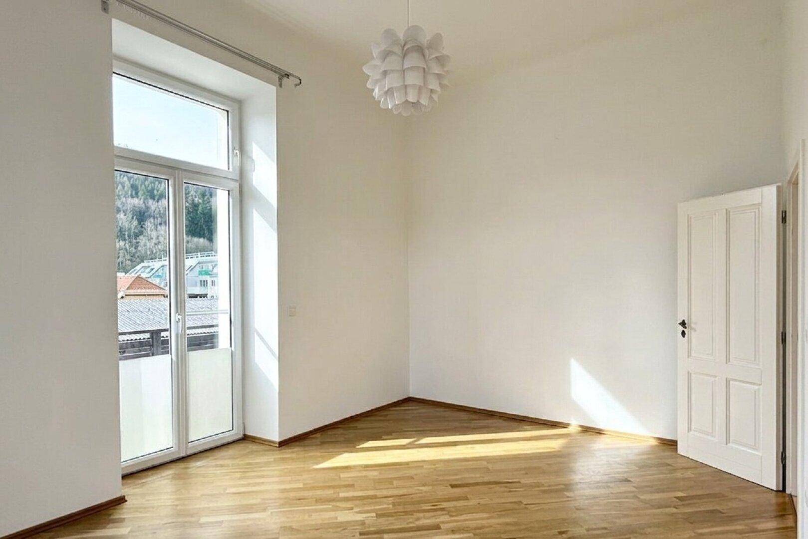 Heller Raum mit Parkettboden und großem Fenster, das einen Blick ins Grüne bietet.