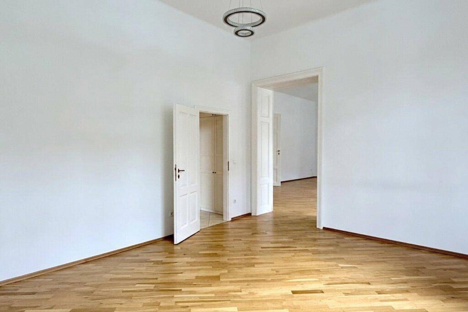 Heller Raum mit Fischgrätparkett und mehreren Türöffnungen, die verschiedene Bereiche verbinden.