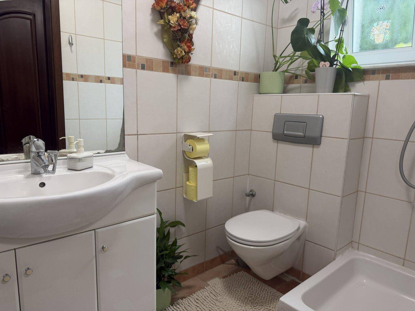 Helles Badezimmer mit Badewanne, Waschbecken, Toilette und einem Fenster für natürliche Belüftung.