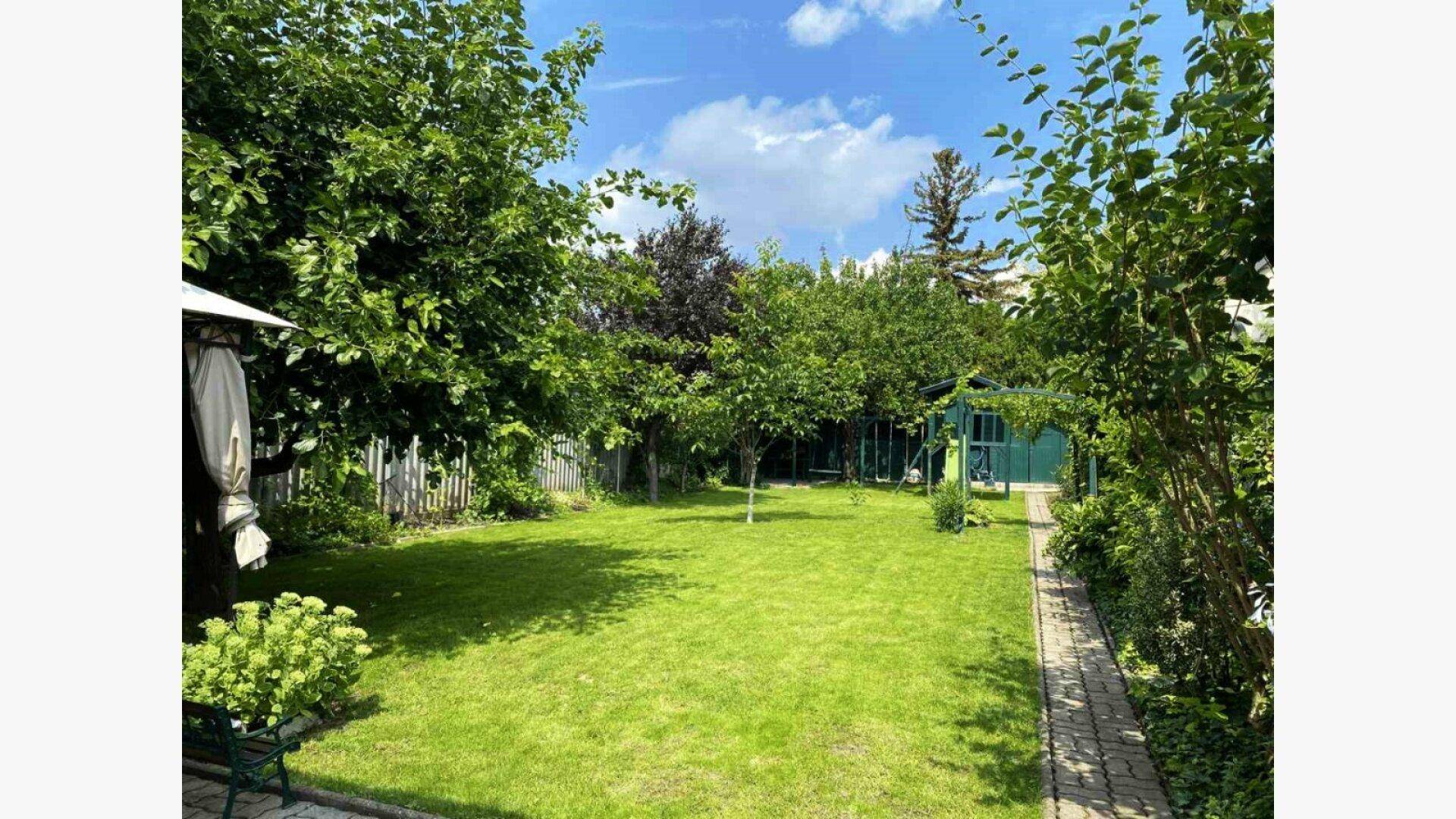 Weitläufiger grüner Garten mit Rasenfläche, vielen Bäumen und einem kleinen Pavillon zum Entspannen.