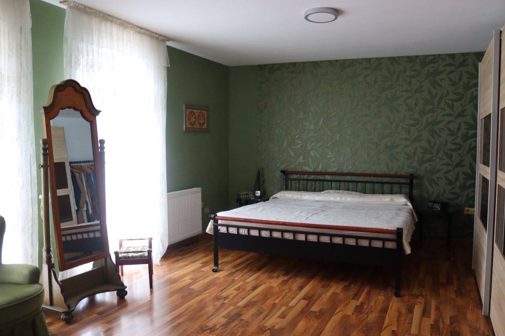 Schlafzimmer mit grün gestrichenen Wänden, einem großen Spiegel und einem bequemen Bett.