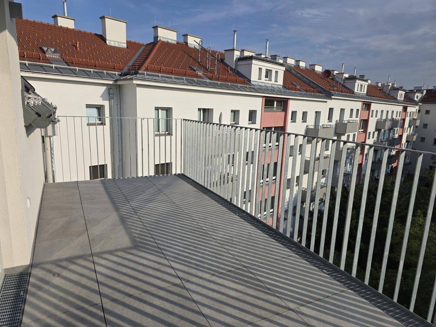 Heller Balkon mit modernem Geländer und Ausblick auf die Dächer der Stadt.