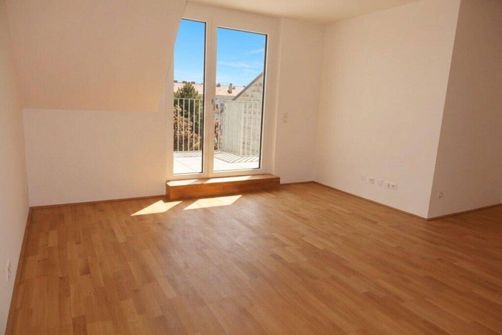 Leerer Raum mit Holzboden und Zugang zu einem kleinen Balkon oder einer Terrasse.