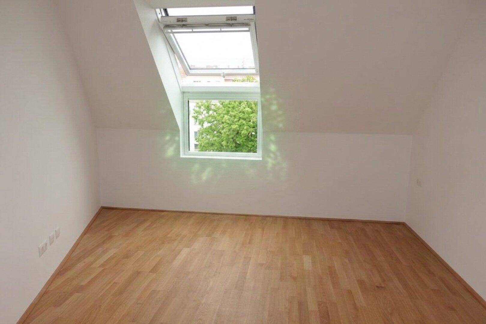 Heller Raum mit Dachschräge, Holzboden und Dachfenster für viel Tageslicht.