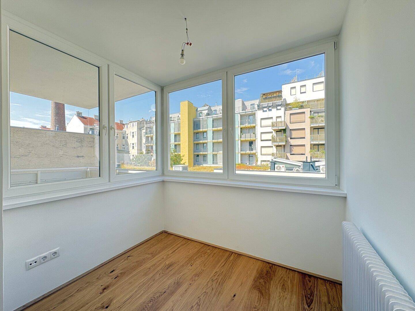 Heller Raum mit Holzboden und großen Fenstern, die einen Blick auf die Stadt bieten.
