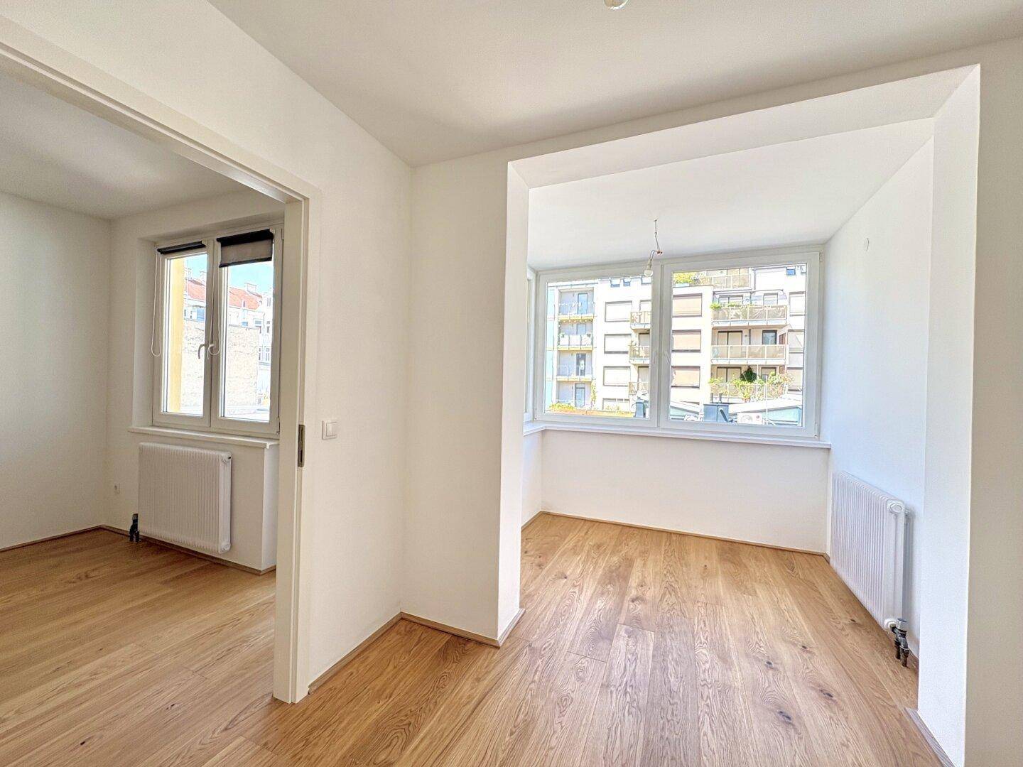 Geräumiger, heller Raum mit Holzboden und Fenstern, die viel Tageslicht hereinlassen.