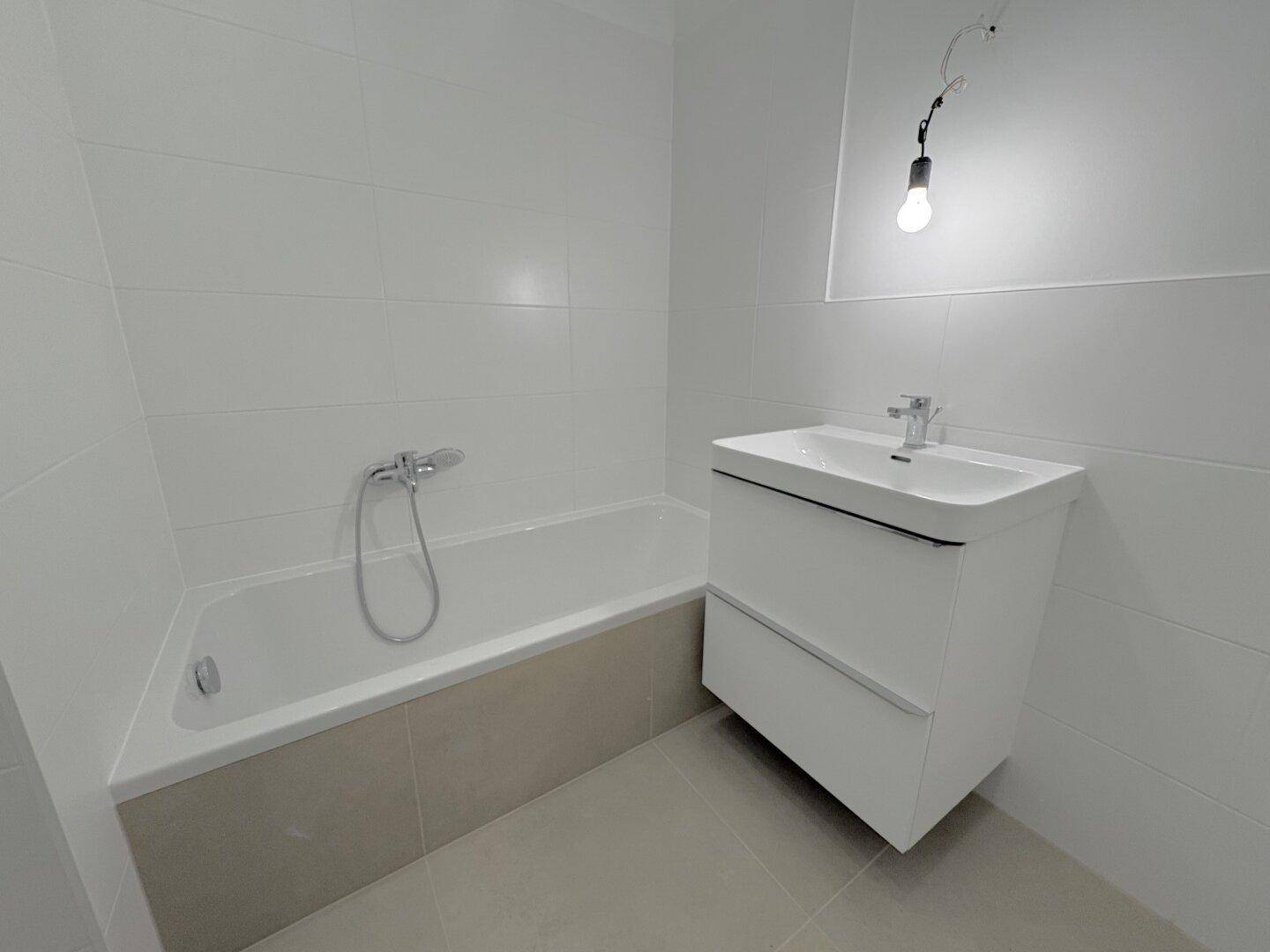 Modernes Badezimmer mit Badewanne, Waschbecken und weißen Fliesen an den Wänden.