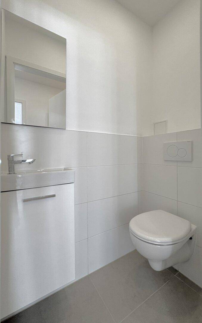 Modernes Gäste-WC mit wandhängender Toilette, Waschbecken und Spiegel.