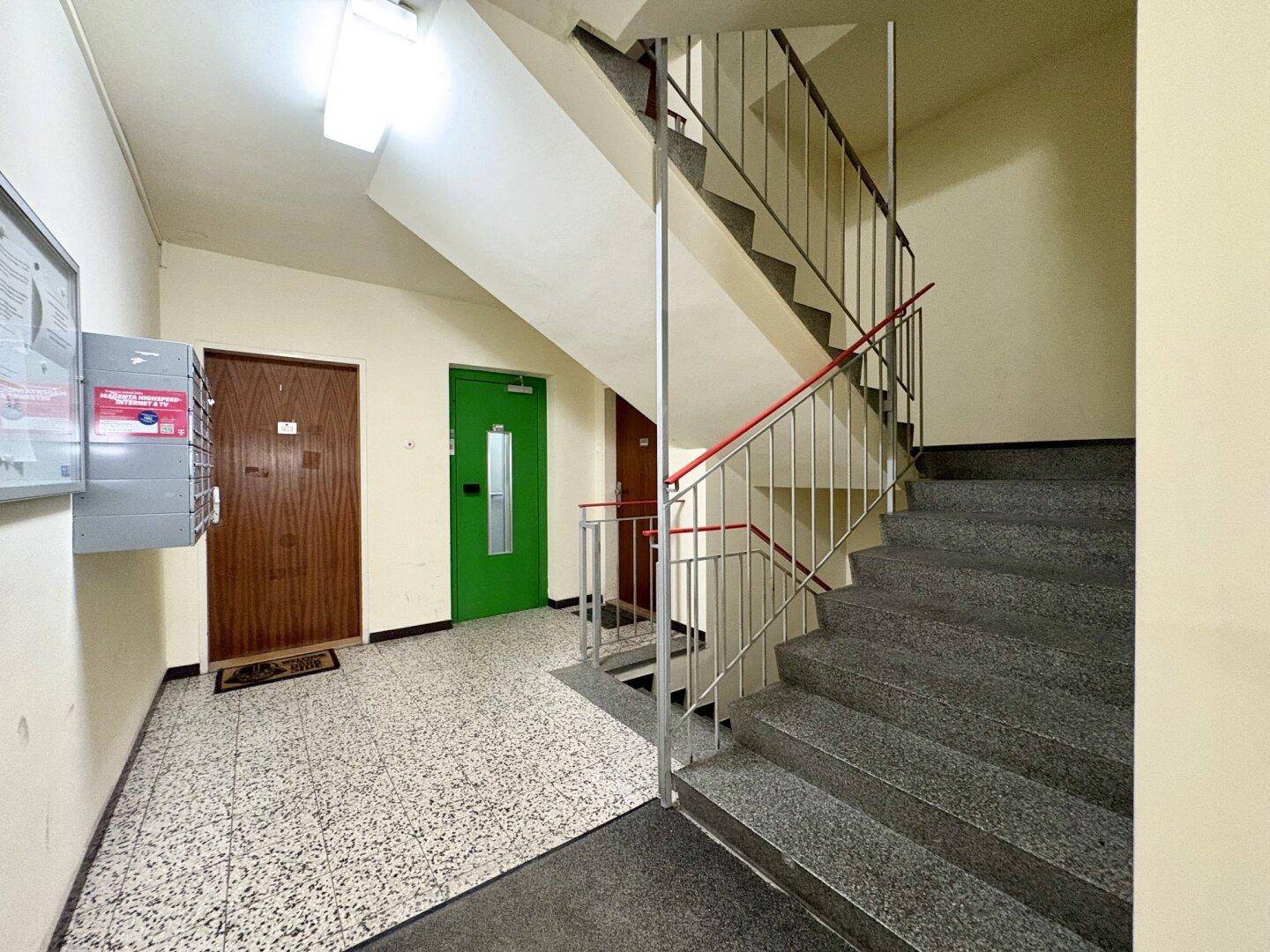 Treppenhaus mit Granitstufen, Geländer und Briefkästen im Eingangsbereich.