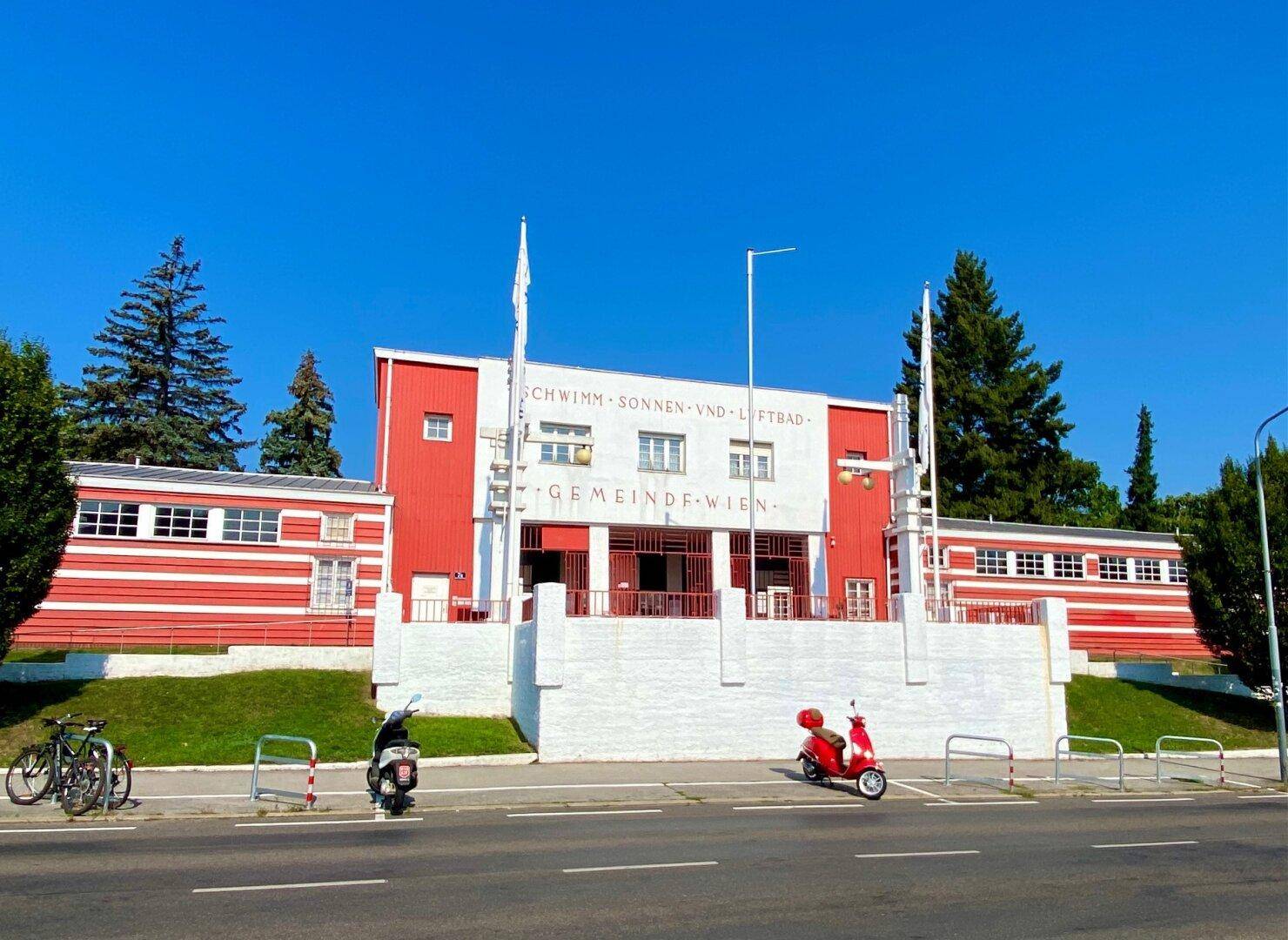 Historisches Schwimmbadgebäude mit markanter roter und weißer Fassade.