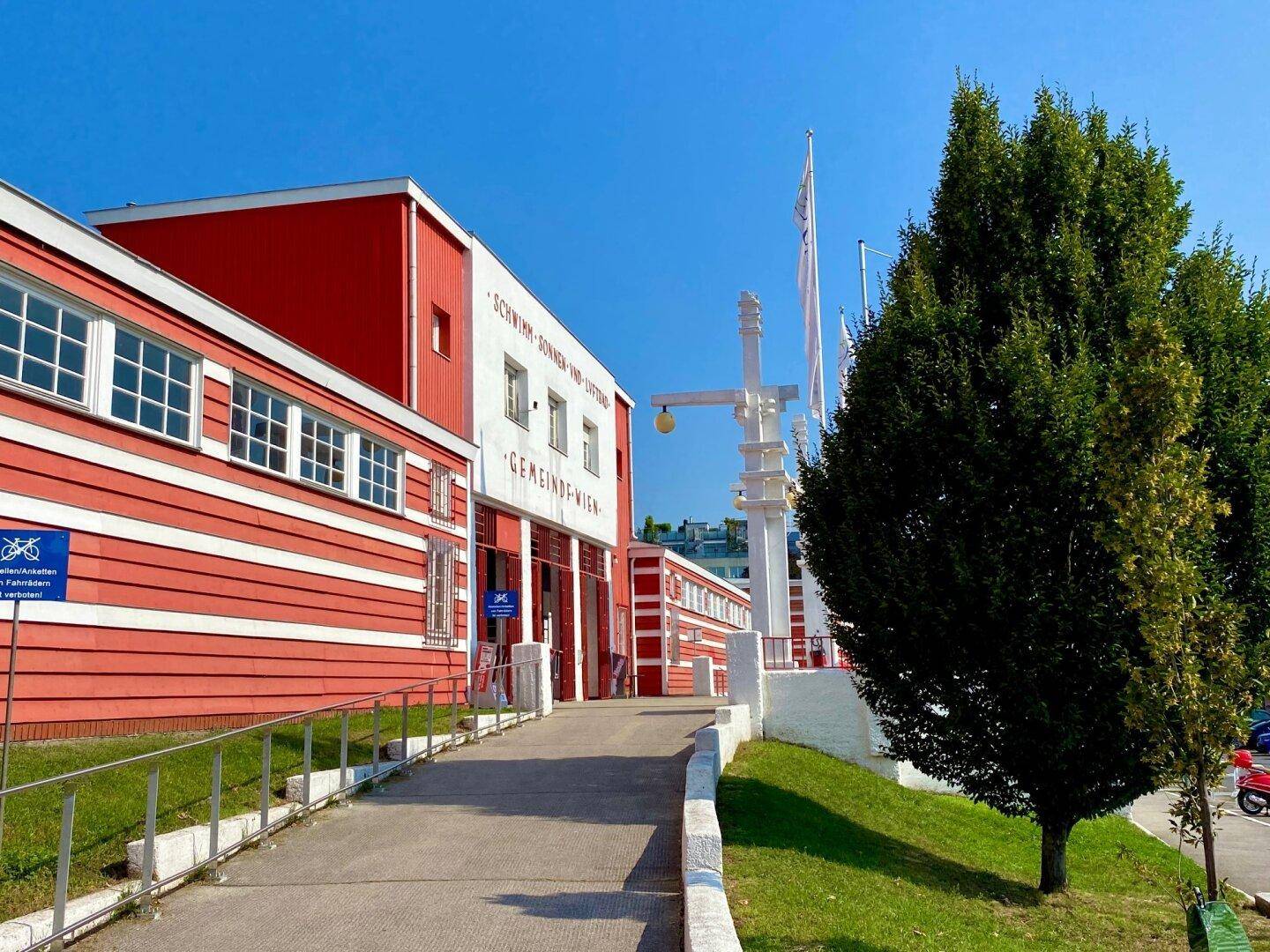 Eingangsbereich eines historischen Schwimmbades mit roter und weißer Fassade.