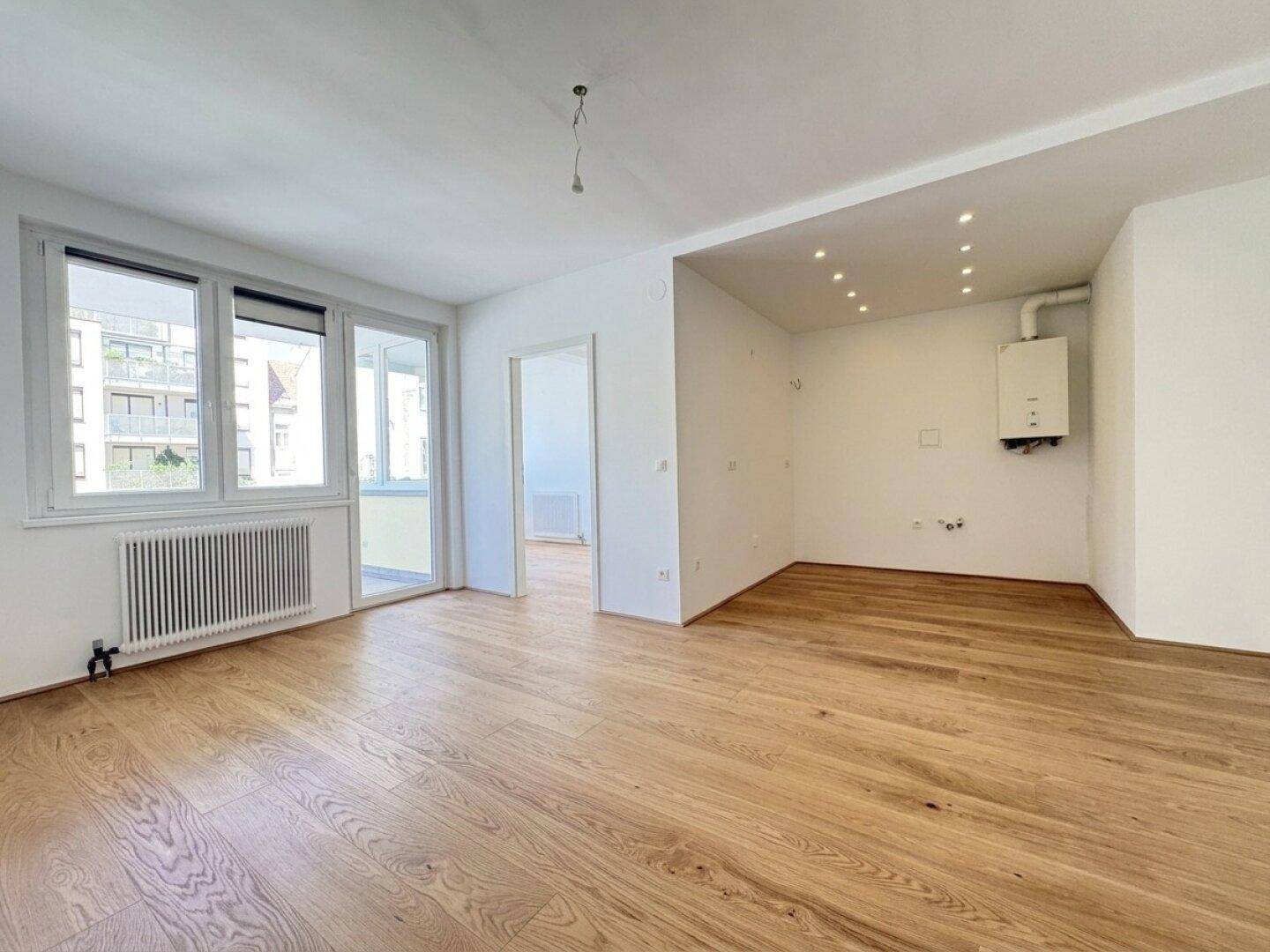 Helles Wohnzimmer mit Holzboden, großen Fenstern und Zugang zu einem Balkon.