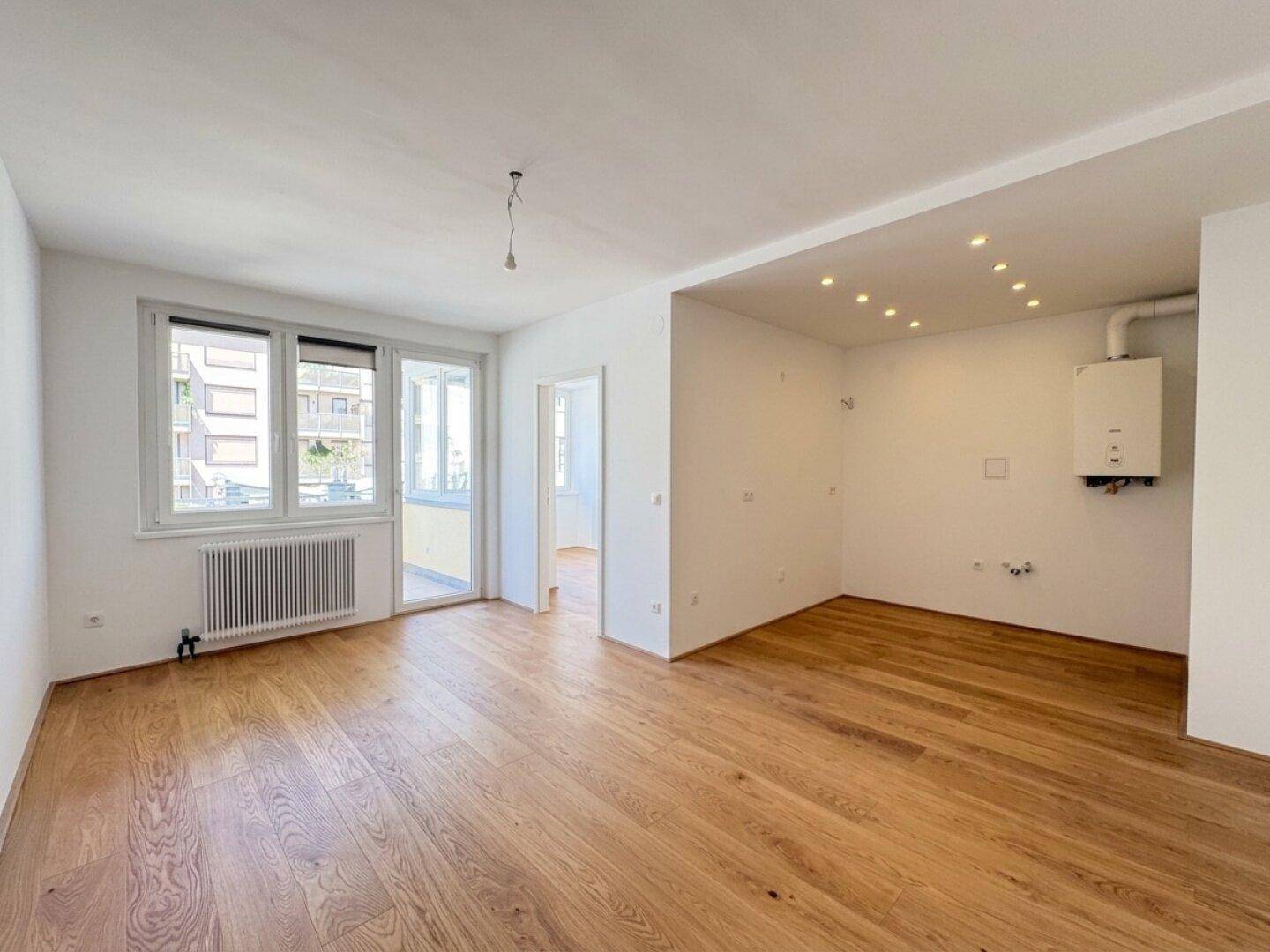 Helles Wohnzimmer mit Holzboden, großen Fenstern und Zugang zu einem Balkon.