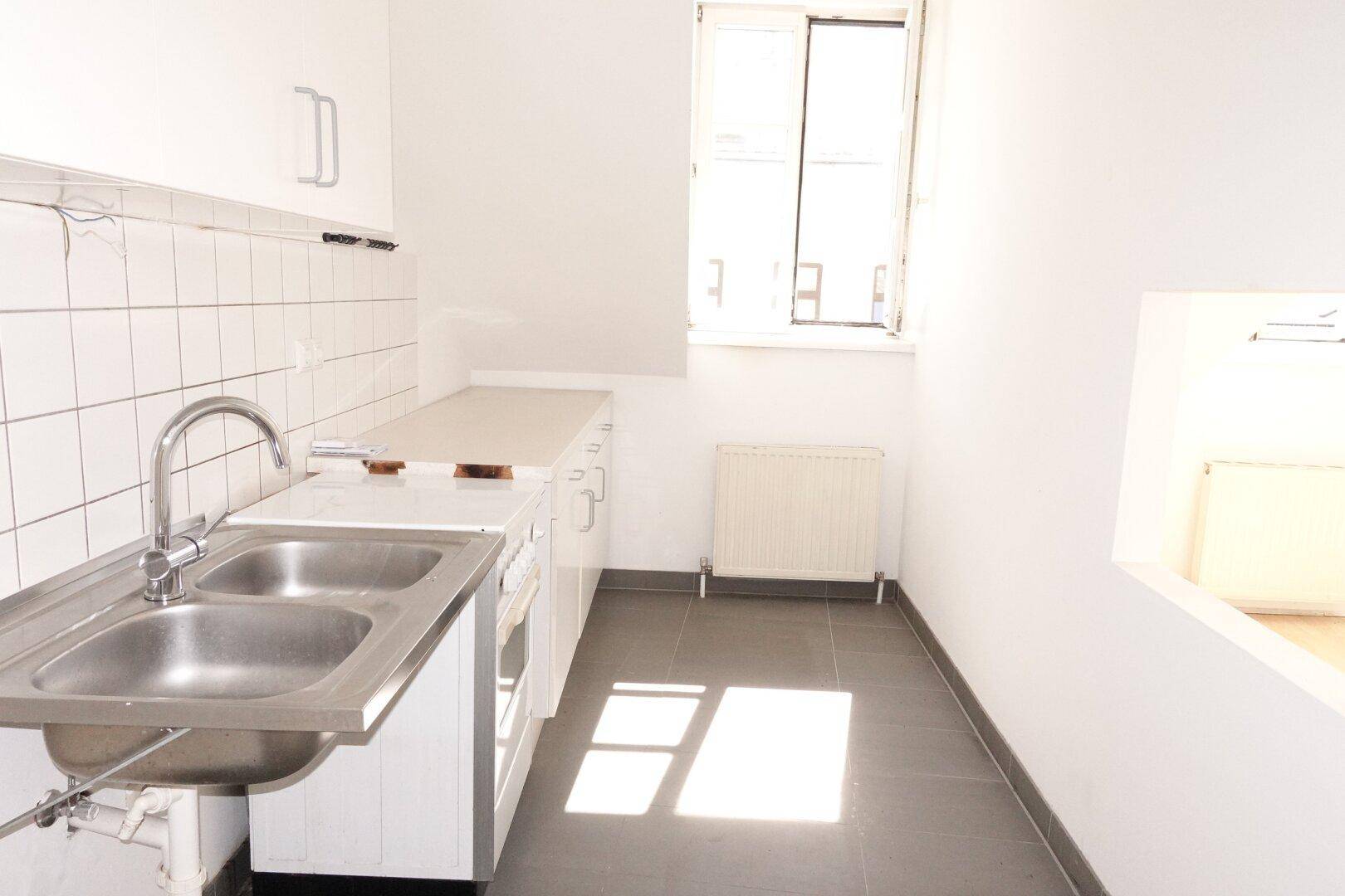 Funktionale Küche mit weißen Unterschränken, Doppelspüle und Fenster, bereit zur Nutzung.