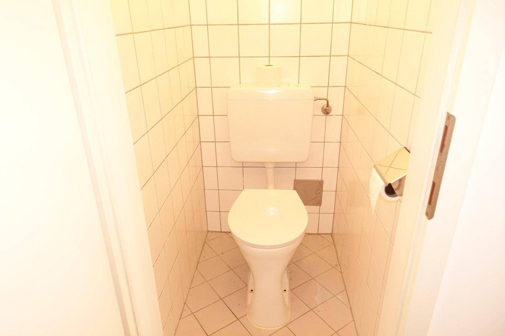Separates WC mit weißer Toilette und hellen Wandfliesen, funktional und sauber.
