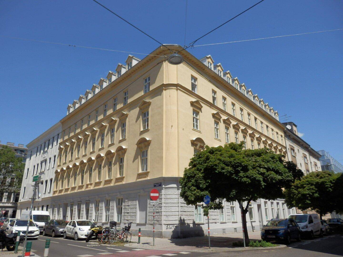 Attraktives Eckgebäude mit gelber Fassade und vielen Fenstern an einer belebten Straße.
