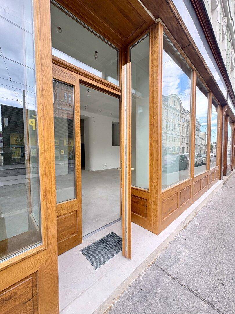 Eingangsbereich eines Geschäfts mit geöffneter Holztür und großen Schaufenstern, die den Blick ins Innere freigeben.