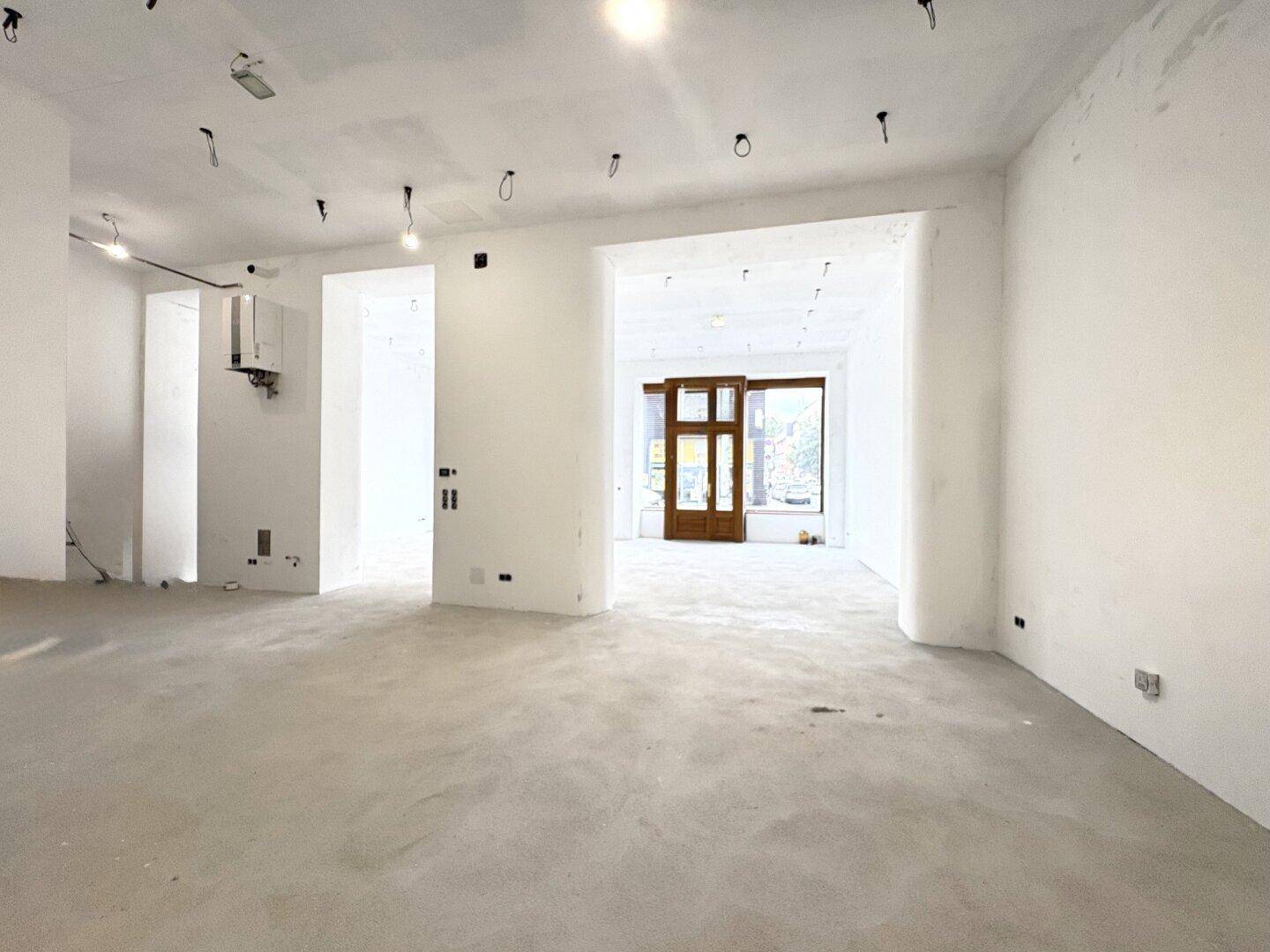 Blick durch den offenen Geschäftsraum zum Eingangsbereich mit den markanten Holzfenstern und Türen.