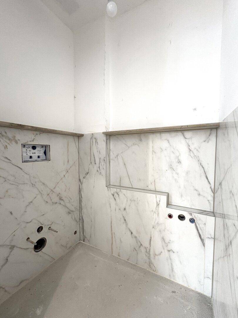 Badezimmer im Bau mit eleganten Marmorfliesen an den Wänden und vorbereiteten Anschlüssen für Armaturen.