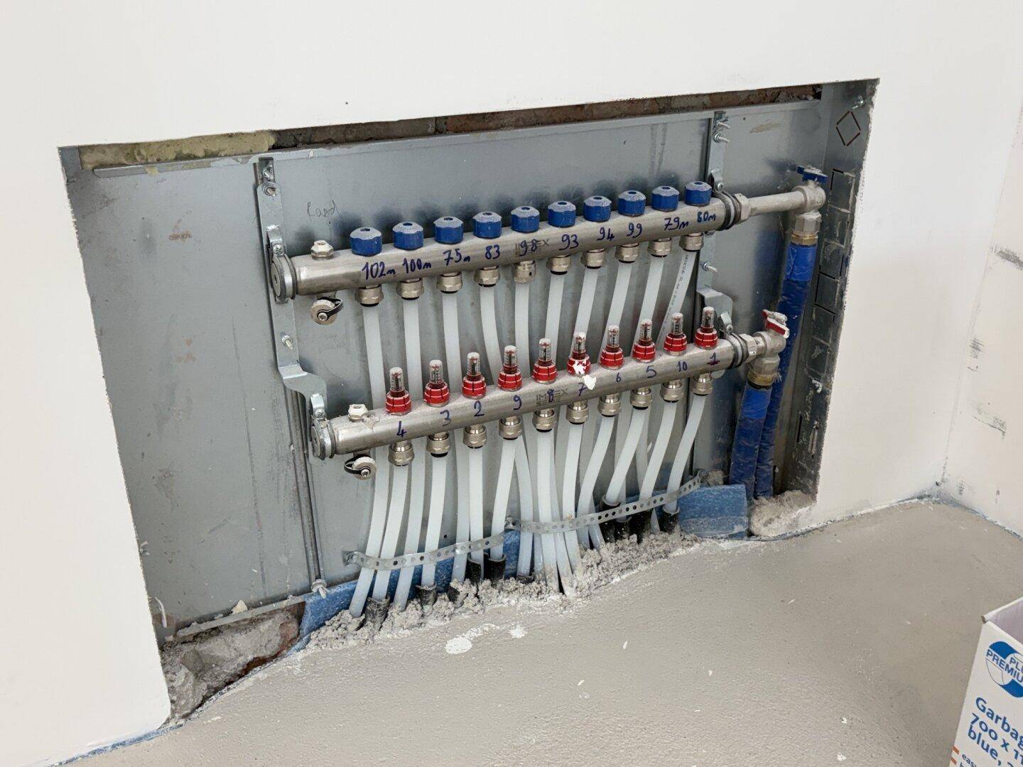 Verteiler für die Fußbodenheizung, sichtbar in einer Wandnische, mit zahlreichen Rohren und Ventilen.
