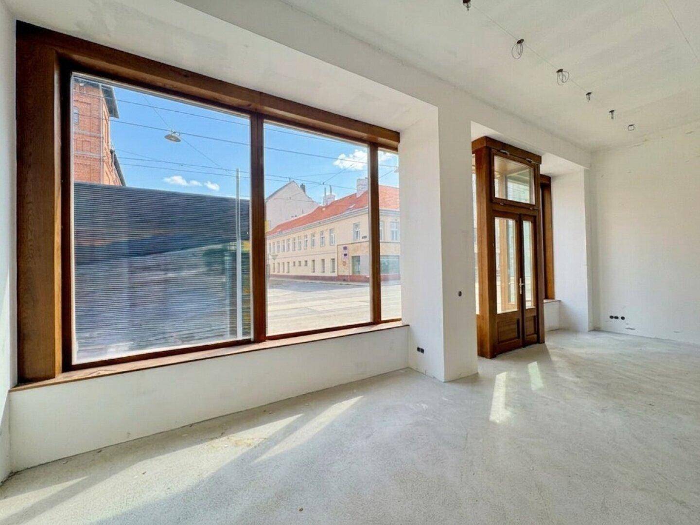 Geräumiger, unmöblierter Geschäftsraum mit großen Fenstern und Holzelementen, die viel Tageslicht hereinlassen.