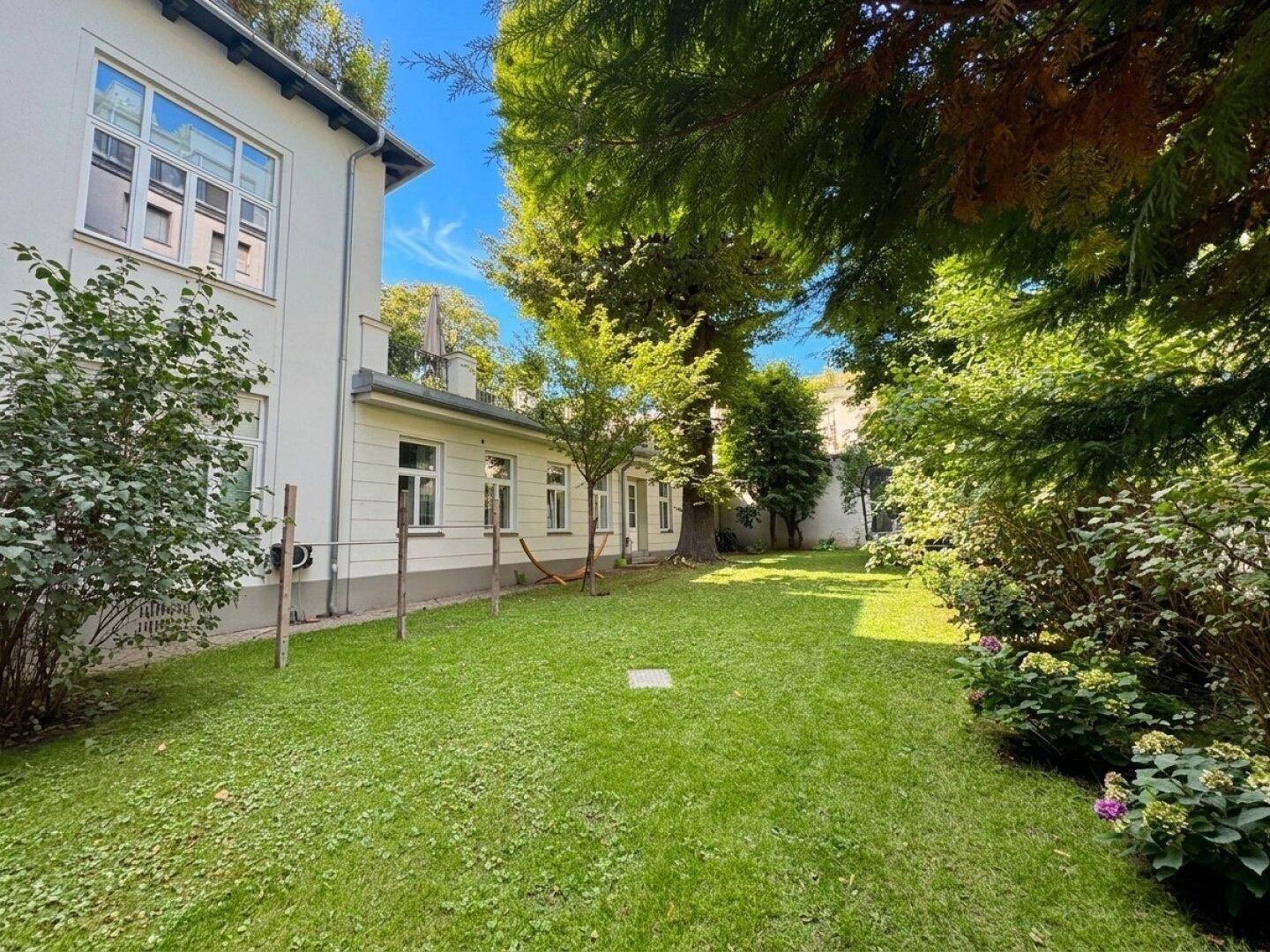 Gepflegter, weitläufiger Gartenbereich mit sattgrünem Rasen und hohen Bäumen, der zum Entspannen einlädt.