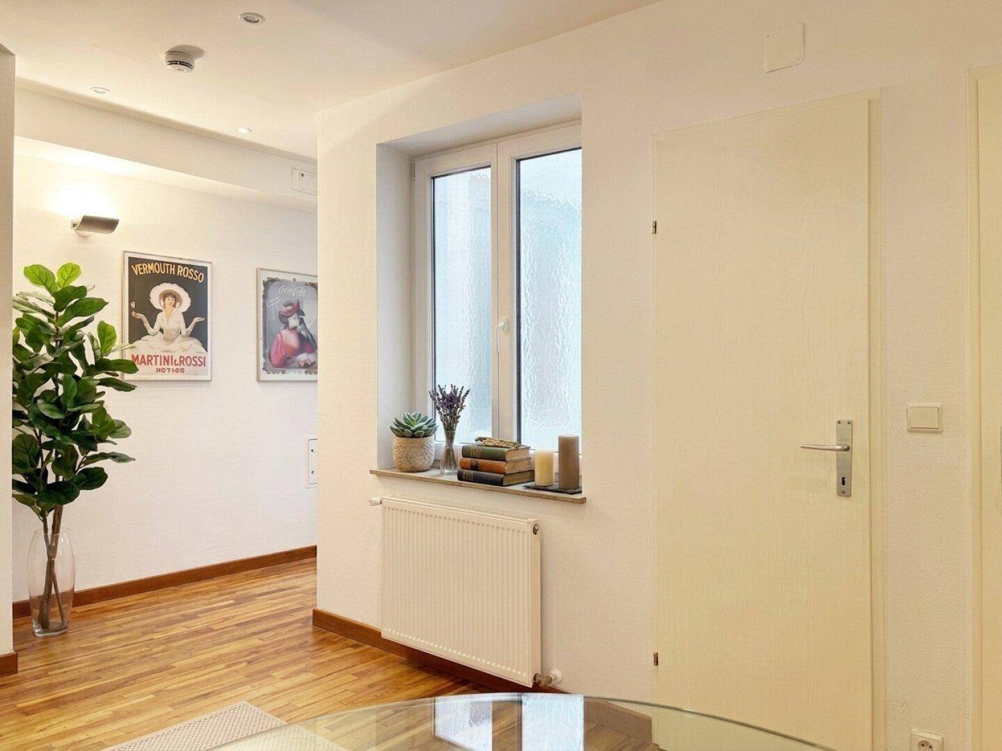 Heller Flur mit Holzboden, Fenster und Heizkörper, geschmackvoll mit Pflanzen dekoriert.