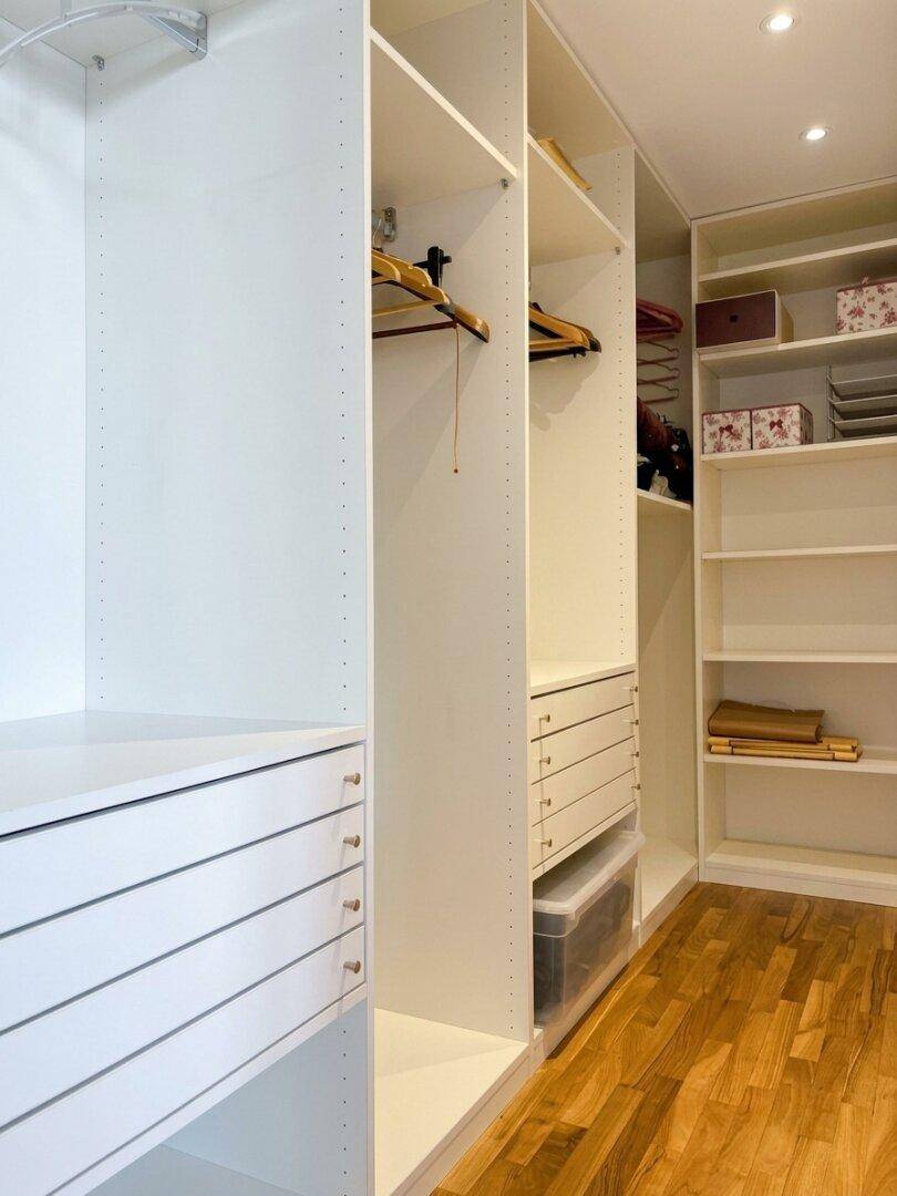 Geräumiger begehbarer Kleiderschrank mit weißen Regalen, Schubladen und Holzboden für optimale Organisation.