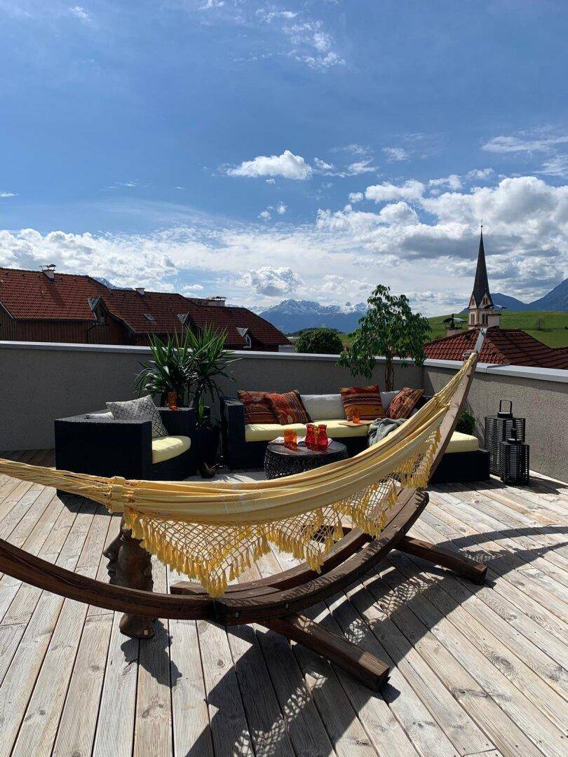 Sonnige Dachterrasse mit Hängematte und Panoramablick auf die umliegende Berglandschaft.