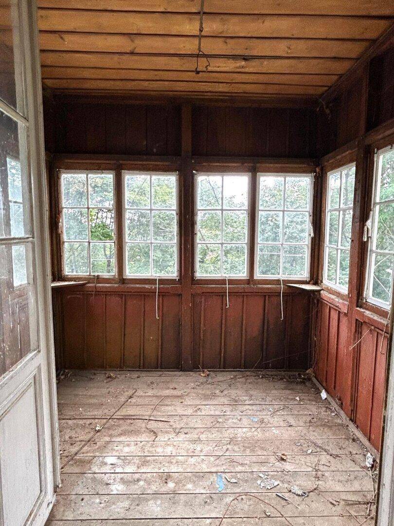 Verglaster Holzveranda-Anbau mit vielen Fenstern und Blick ins Grüne.