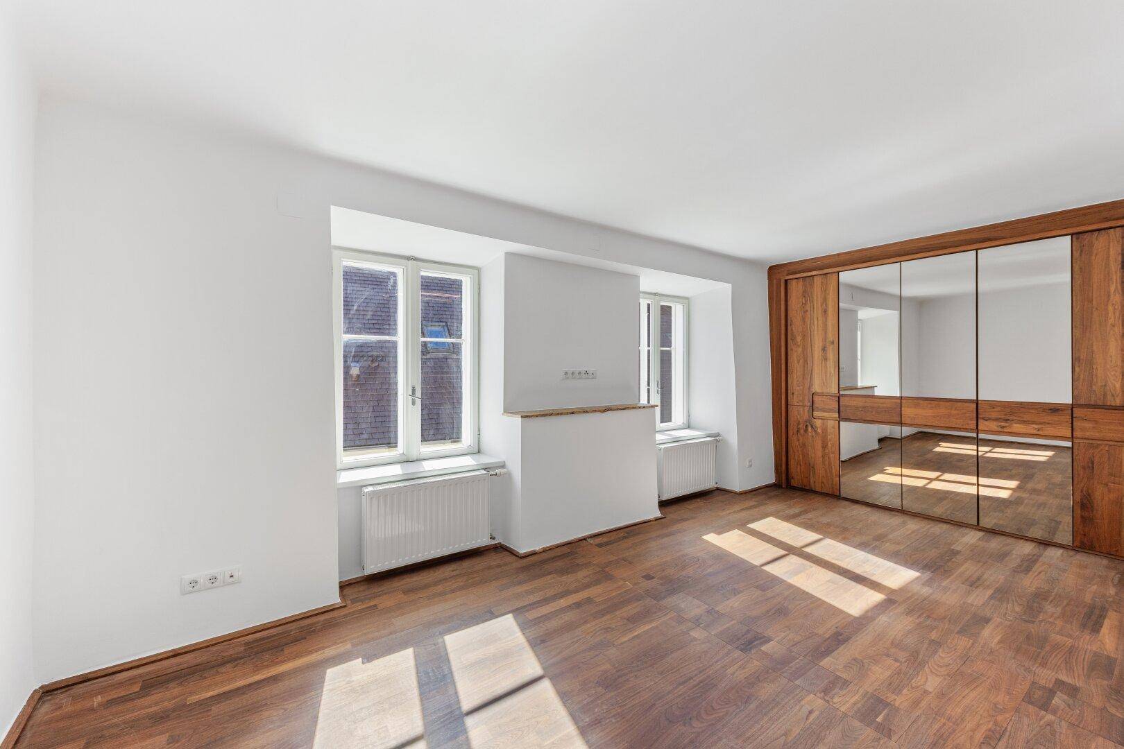 Geräumiges, leeres Schlafzimmer mit Holzboden und elegantem Spiegelschrank.
