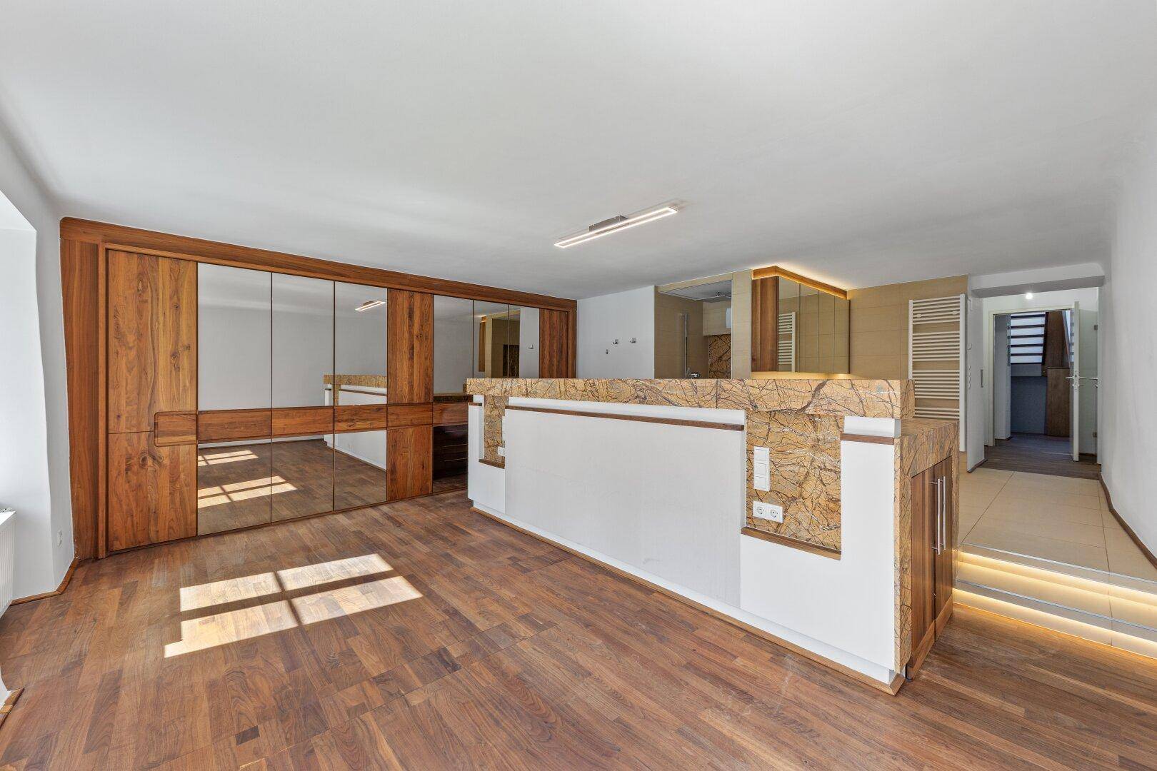Geräumiges Hauptschlafzimmer mit Holzboden, Spiegelschrank und offenem Übergang zum Bad.