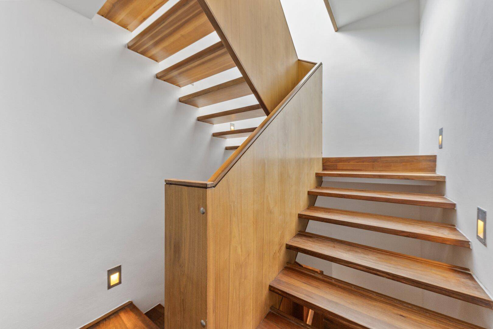 Elegante Holztreppe mit integrierter Beleuchtung, die verschiedene Ebenen verbindet.