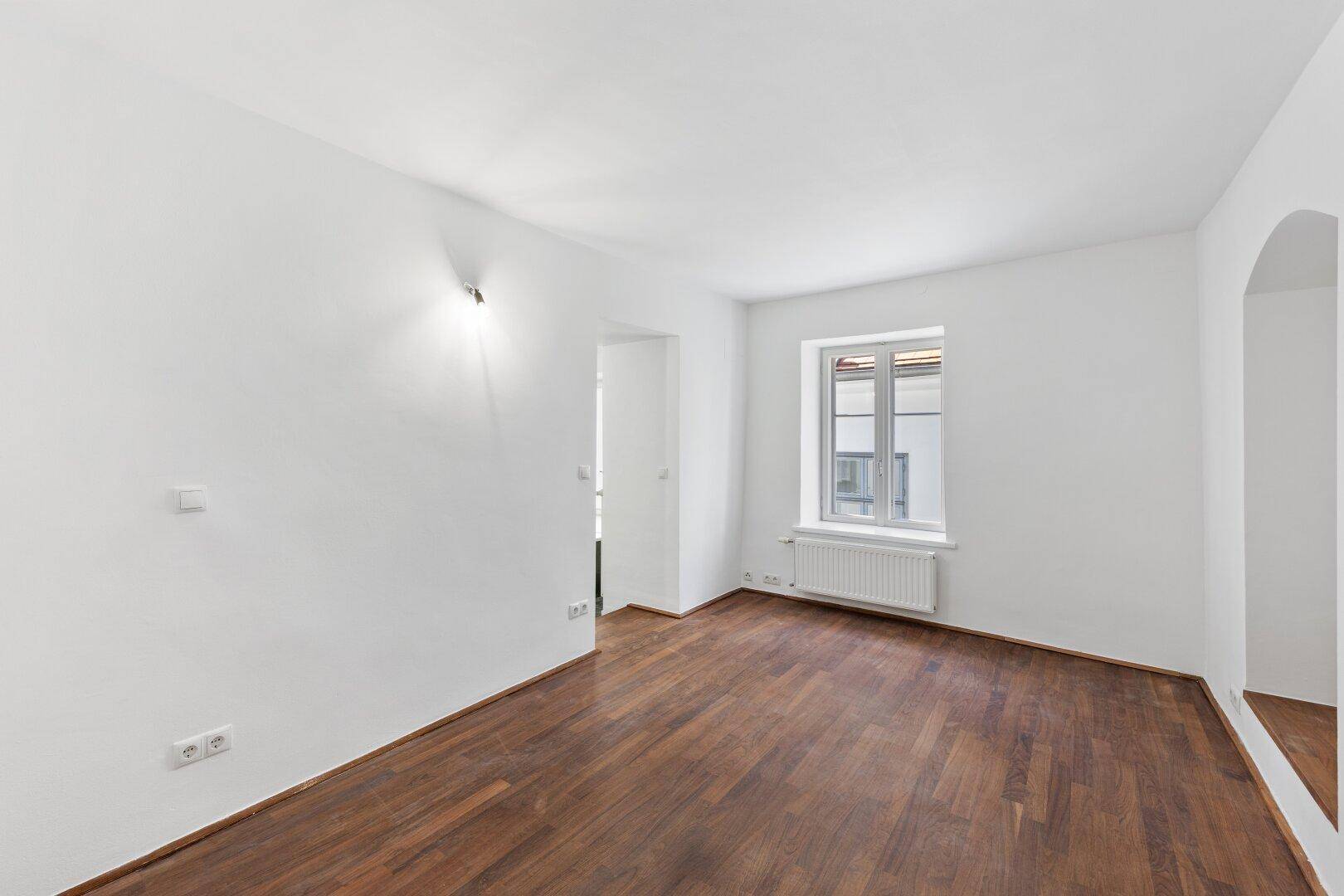 Helles, leeres Schlafzimmer mit Holzboden und einem Fenster.