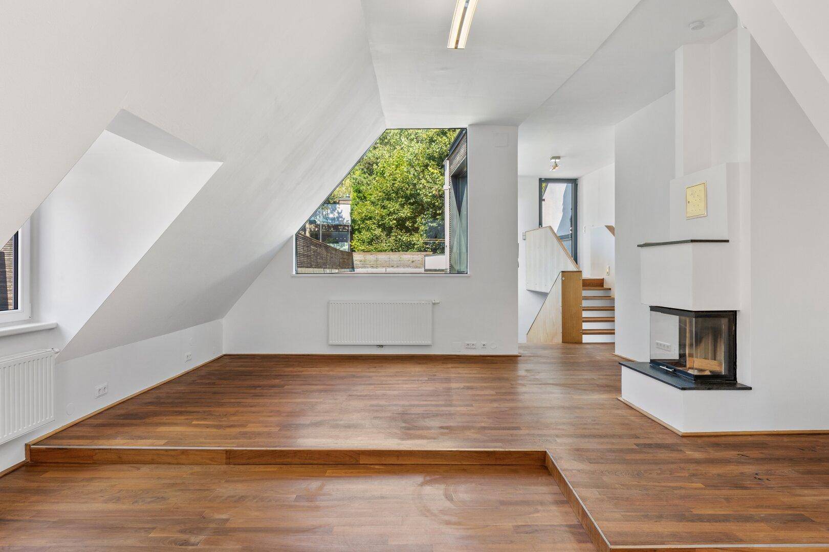 Geräumiges, leeres Dachgeschoss-Wohnzimmer mit Kamin und warmem Holzboden.