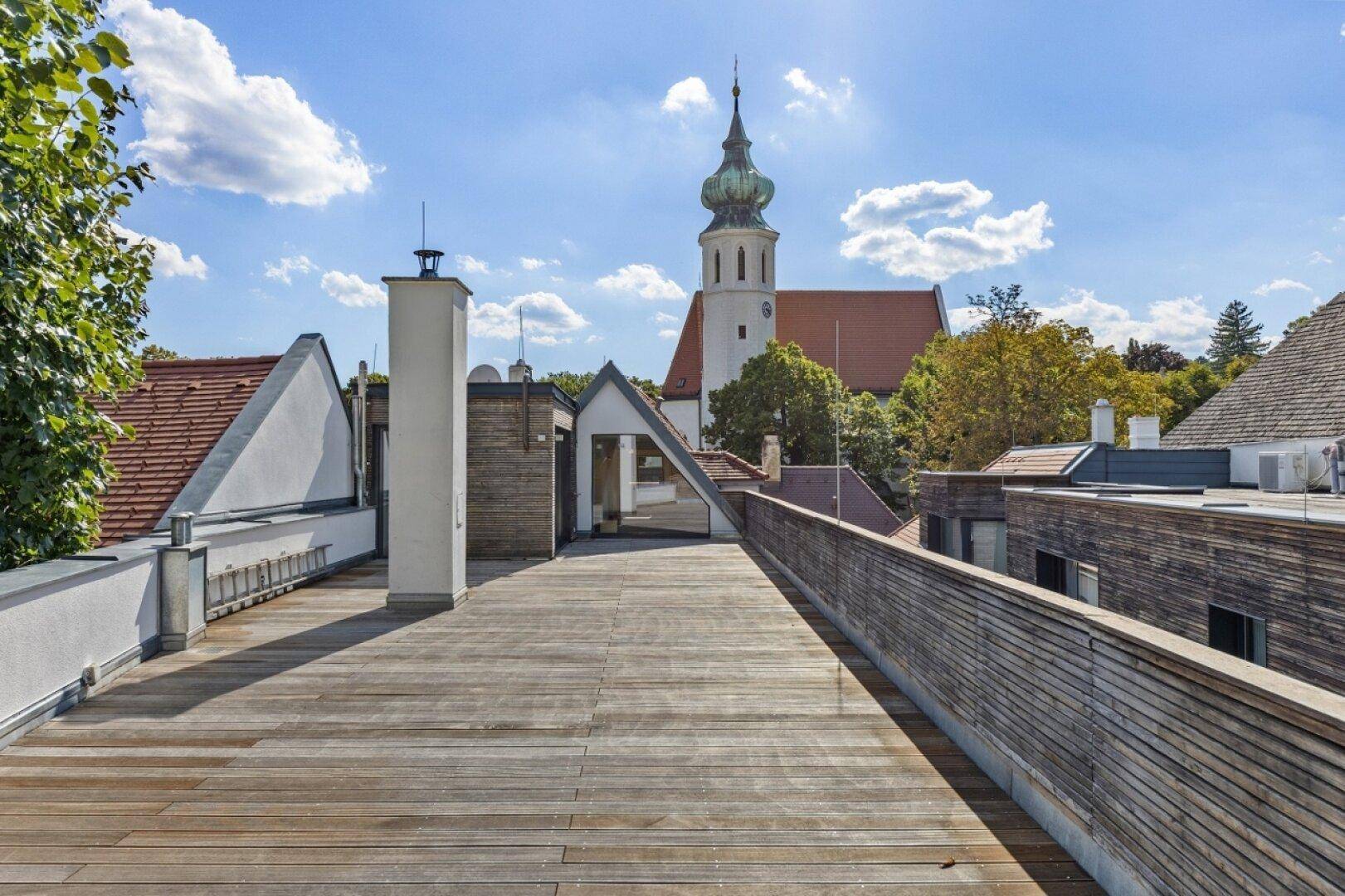 Weitläufige Dachterrasse mit Holzboden und freiem Blick auf die umliegende Architektur und Kirche.