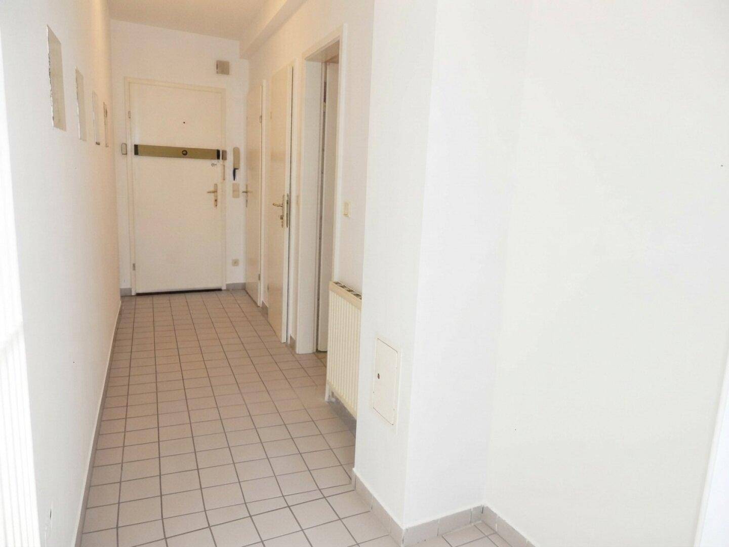Eingangsbereich mit Fliesenboden, weißen Wänden und der Haupttür, die zu den Wohnräumen führt.