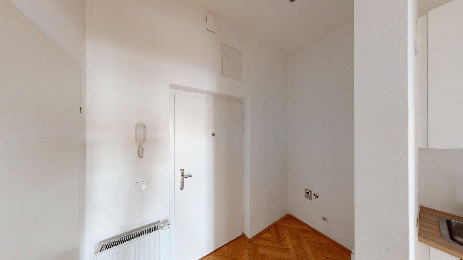 Eingangsbereich mit Parkettboden, weißer Tür und Anschlussmöglichkeiten für eine Waschmaschine.