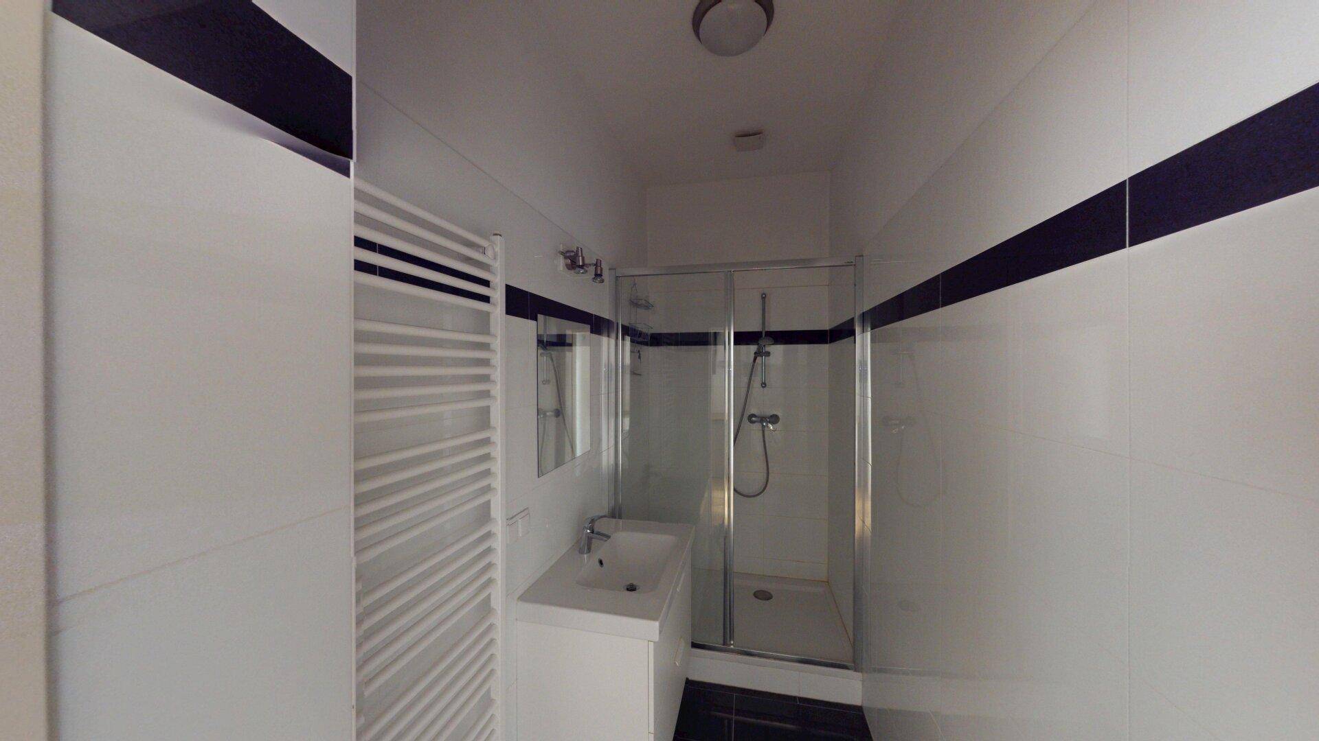 Modernes Badezimmer mit weiß-blauen Fliesen, Duschkabine und beheiztem Handtuchhalter.
