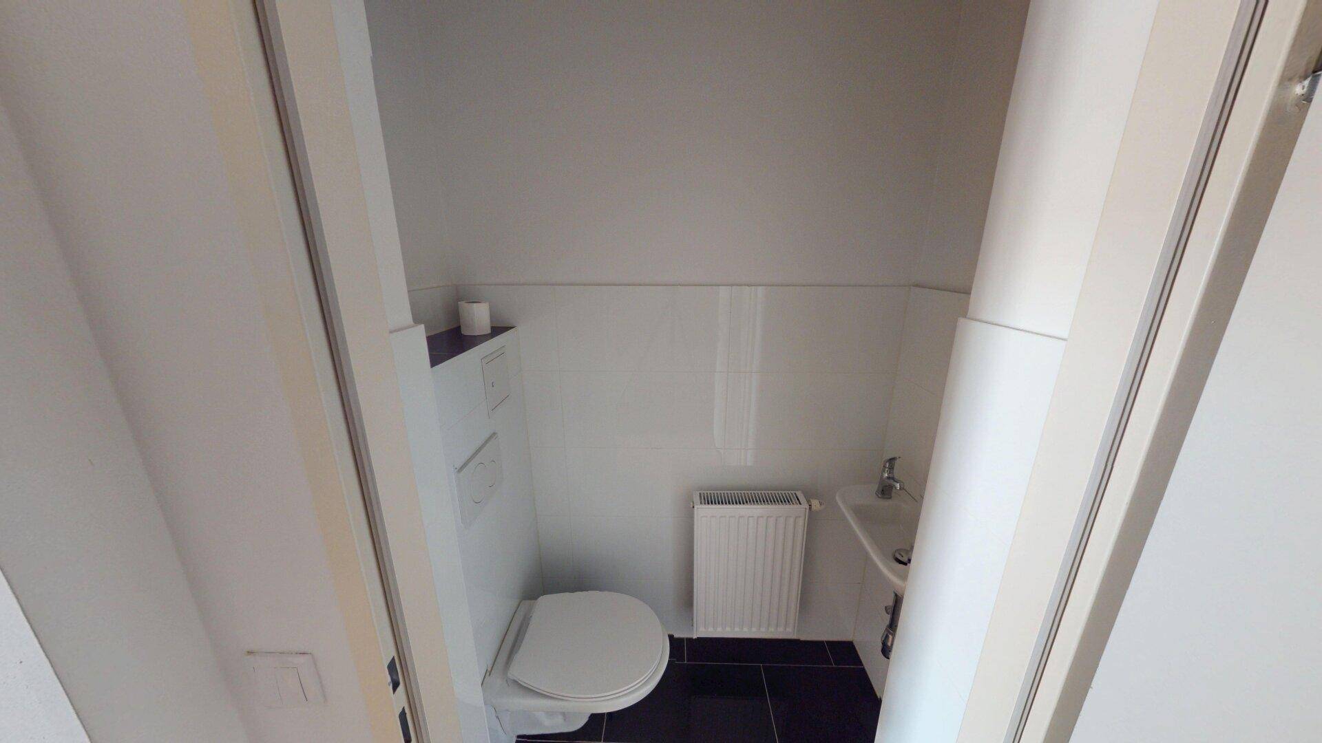 Kleines separates WC mit Toilette, Handwaschbecken und dunklem Fliesenboden.