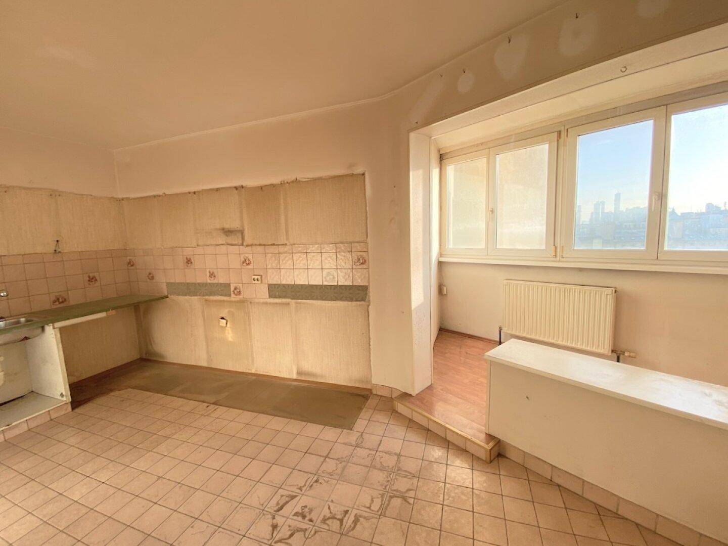 Renovierungsbedürftige Küche mit alten Fliesen, fehlenden Schränken und Blick nach draußen.