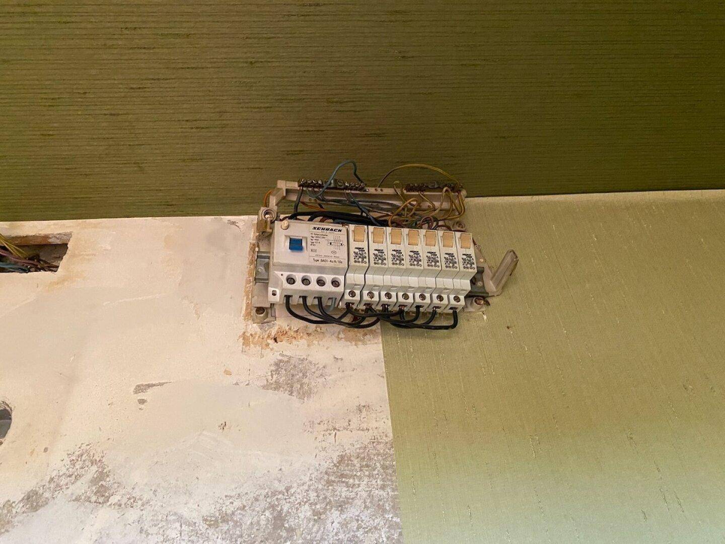 Freiliegender Sicherungskasten und elektrische Installationen an einer Wand, die renoviert werden muss.